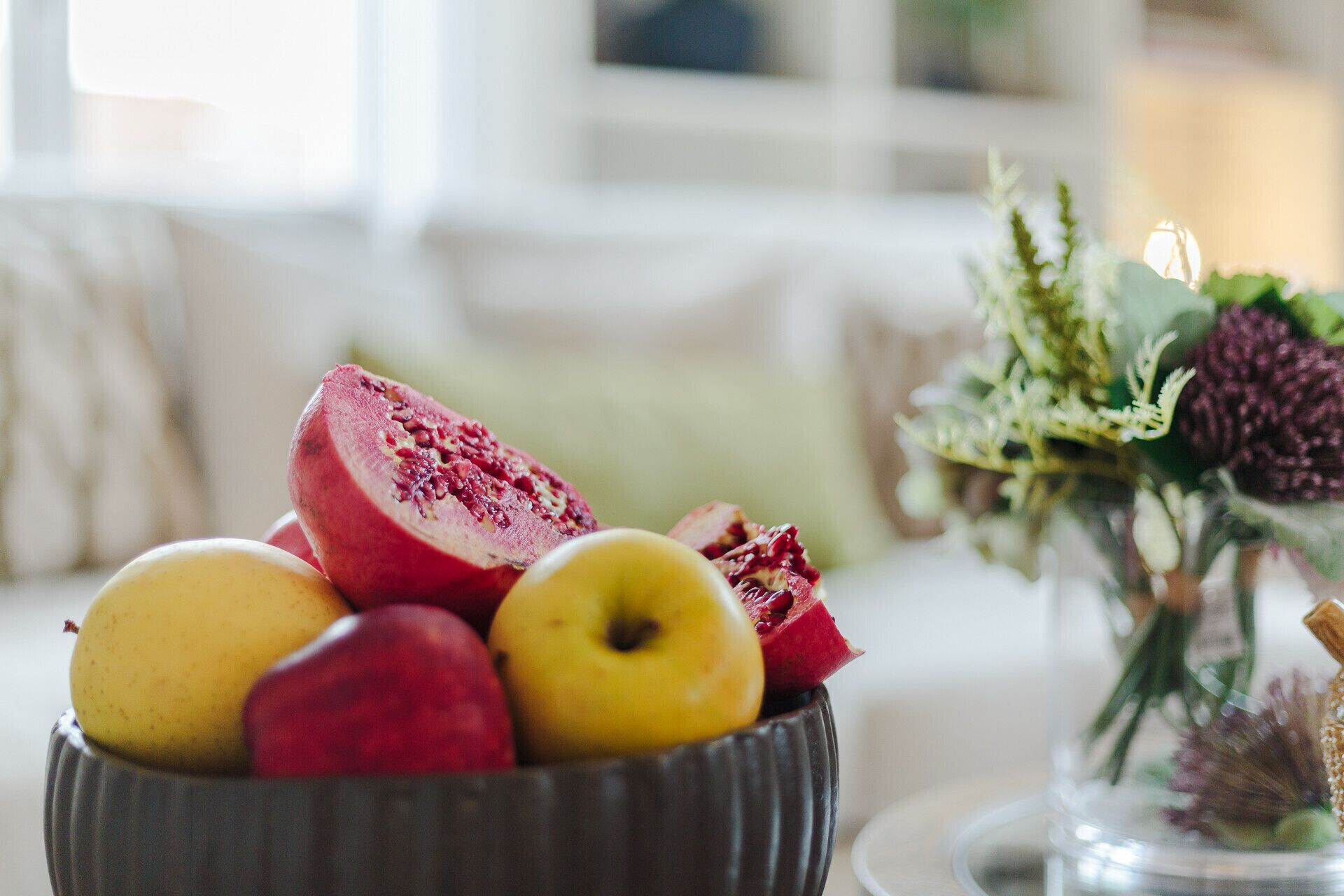A bowl of fruits including pomegranate, apples, and pears on a table.