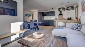 Ein modernes Wohnzimmer mit einer Couch, einem Esstisch und Stühlen. Es gibt eine Küchenzeile mit Schränken und einer Mikrowelle.