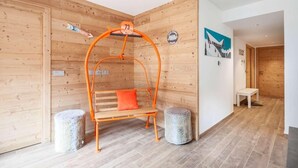 Ein Holzinnenraum mit einer hölzernen Bank unter einem orangefarbenen Bogen, zwei Stehsesseln und einer Holztür mit einem Nummernzeichen.