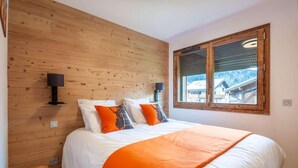 Ein Schlafzimmer mit einem Holz-Kopfteil, einem großen Fenster mit Blick und einem Bett mit weißer und orangefarbener Bettwäsche.