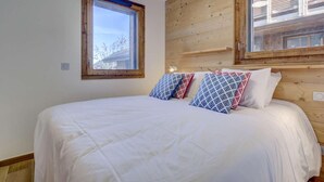 A bedroom with a large bed, two windows, and wooden paneling on the walls. - 140m from ski lifts, 1st floor, terrace, tv, 77m², Morzine (Morzine)