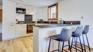 A modern kitchen with white cabinetry, a built-in oven, a coffee machine, and a small island with bar stools. - 140m from ski lifts, 1st floor, terrace, tv, 77m², Morzine (Morzine)