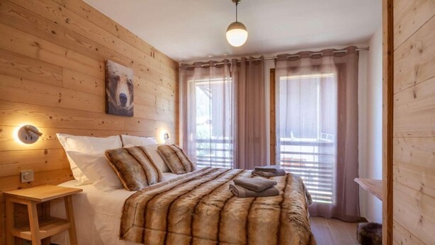 Camera da letto con rivestimento in legno, un letto, comodini e un tavolino da notte.