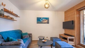 Un soggiorno moderno con un divano blu, un tavolino rotondo e un televisore piatto montato su una parete in legno.