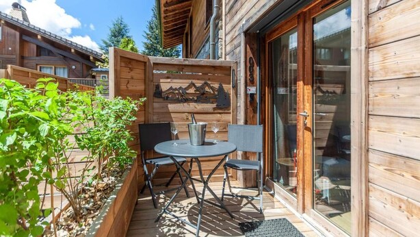 A wooden cabin with a patio area featuring a table and chairs, a metal bucket, and a glass door leading inside. - 140m from ski lifts, balcony, tv, 27m², Morzine (Morzine)