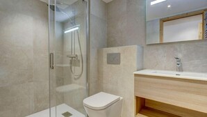 A modern bathroom with a glass-enclosed shower, a white toilet, and a wooden vanity with a mirror above it.