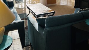Un salon avec un canapé, une table basse et un téléviseur. Il y a un balcon avec une table et des chaises, ainsi qu’une fenêtre avec des rideaux.