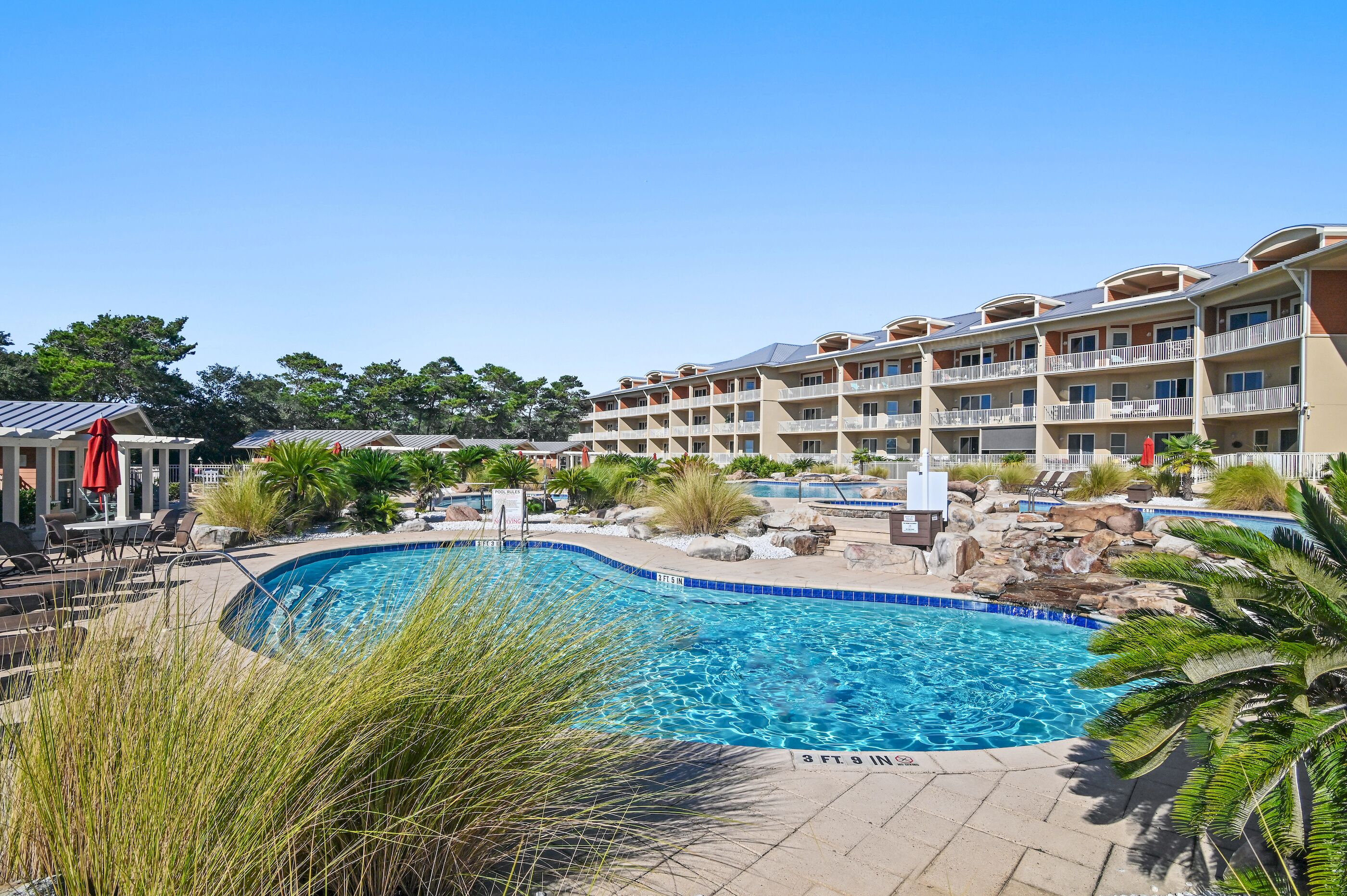 A hotel with a swimming pool, outdoor seating, and a landscaped area with rocks and plants.