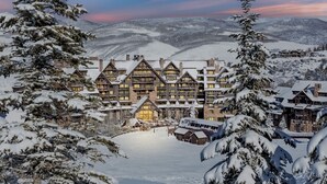 Un gran alojamiento de varias plantas con un estilo arquitectónico tradicional, rodeado de árboles y colinas nevadas.