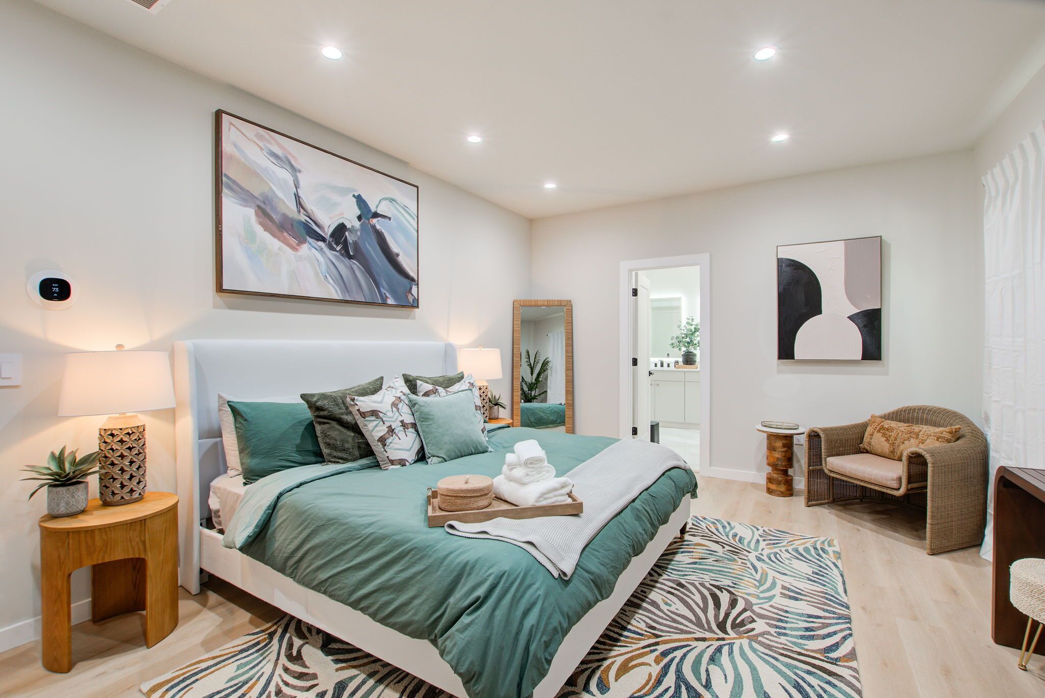 A modern bedroom with a large bed, a bedside table with a lamp, a mirror, and a chair.