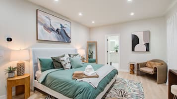 A modern bedroom with a large bed, a bedside table with a lamp, a mirror, and a chair.