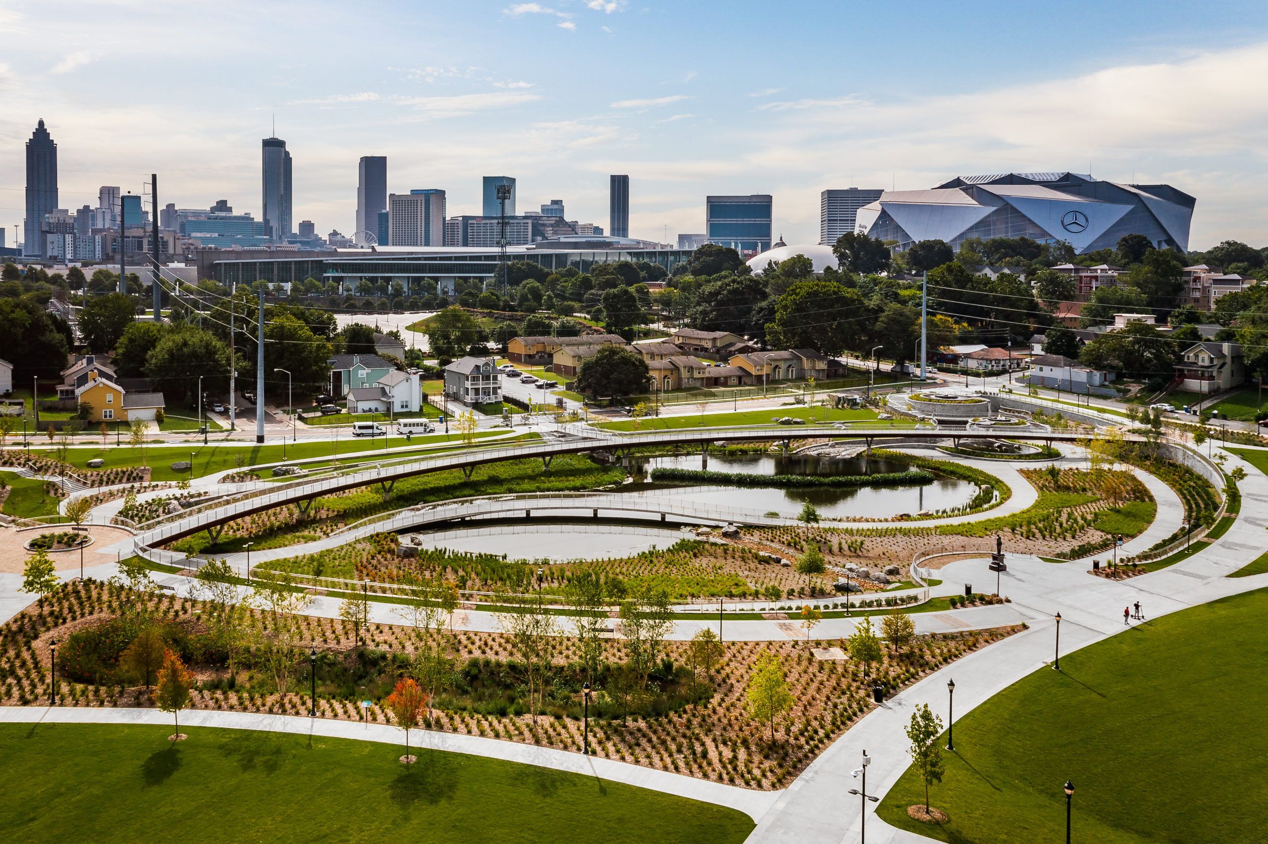A landscaped urban area with a modern building, bridges, and a city skyline in the background.