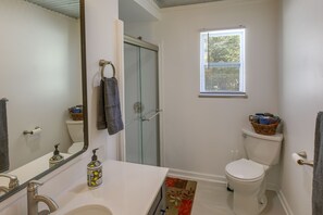 A bathroom with a white sink, a mirror, a toilet, a shower door, and a window. - Rustic Whitwell Home w/ Grill, Near State Parks! (Whitwell)