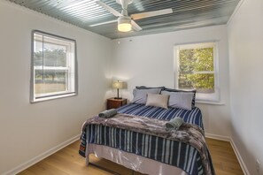 A bedroom with a bed, two windows, a nightstand, a lamp, and a ceiling fan. - Rustic Whitwell Home w/ Grill, Near State Parks! (Whitwell)