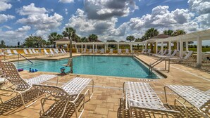 A swimming pool with lounge chairs and umbrellas, surrounded by a covered area with a clear view of the sky. - Golfer's Paradise: Pet-Friendly Home in Wildwood (Wildwood)