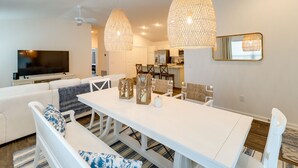 A modern living room with a white sofa, a dining table with chairs, and pendant lights. - Golfer's Paradise: Pet-Friendly Home in Wildwood (Wildwood)