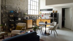 Una cocina moderna con un amplio ventanal, armarios de madera y un comedor con sillas blancas.