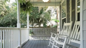 Une véranda avec des balustrades blanches, une chaise berçante et un banc.