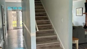 Un couloir avec un escalier en bois, une porte au fond et un mur bleu clair.