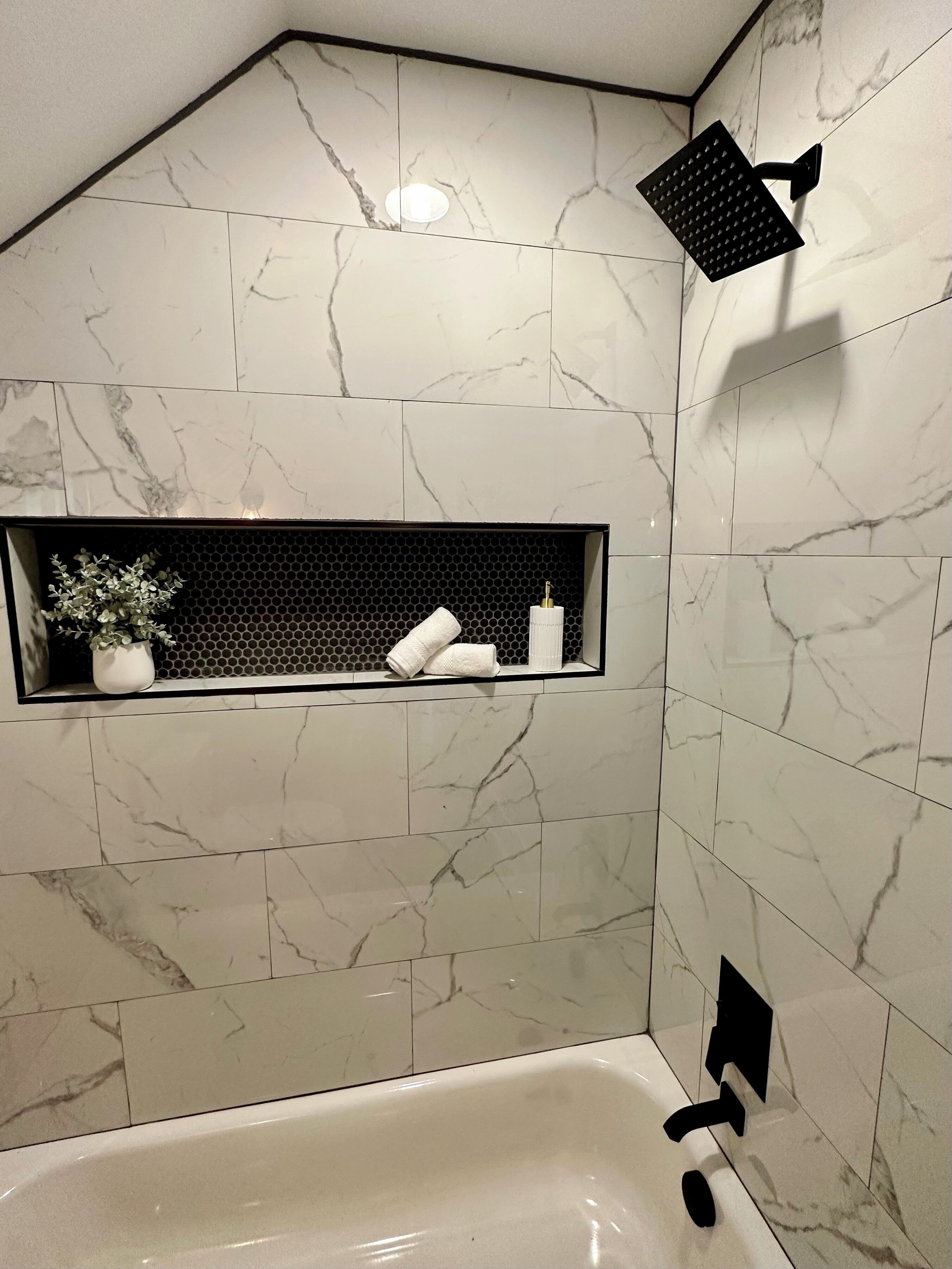 A bathroom with a bathtub, a shower head, and a shelf with toiletries.