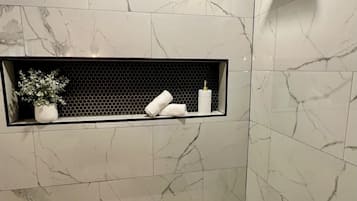 A bathroom with a bathtub, a shower head, and a shelf with toiletries.