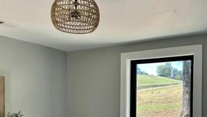 A bedroom with a large window, a wooden dresser, a bedside plant, and a woven ceiling light fixture. - Cottage at the Ridge#2-40 min south of Nashville (Spring Hill)