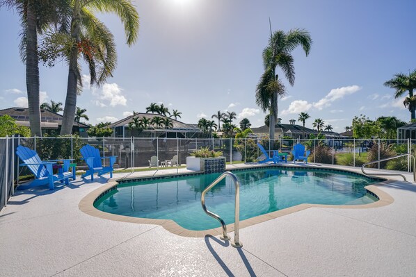 A swimming pool with blue chairs and palm trees. - Dock, Grill & Pool: Waterfront Cape Coral Home! (Cape Coral)