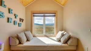 A cozy room with a loft bed, a large window with a view of a grassy field, and the words "LET IT SNOW" on the wall. - Hot Tub & Fire Pit: Idyllic Getaway in Angel Fire! (Angel Fire)
