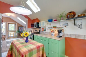 A kitchen with green cabinets, a microwave, a stove, and a coffee maker. There is a window with a view of trees and a door leading to another room. - Charming Livingston Vacation Rental w/ Views! (Livingston)