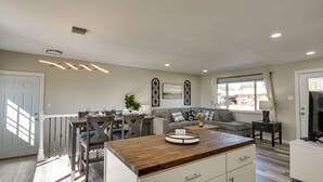Una cocina moderna con encimera de madera, armarios blancos y comedor con mesa y sillas grises.