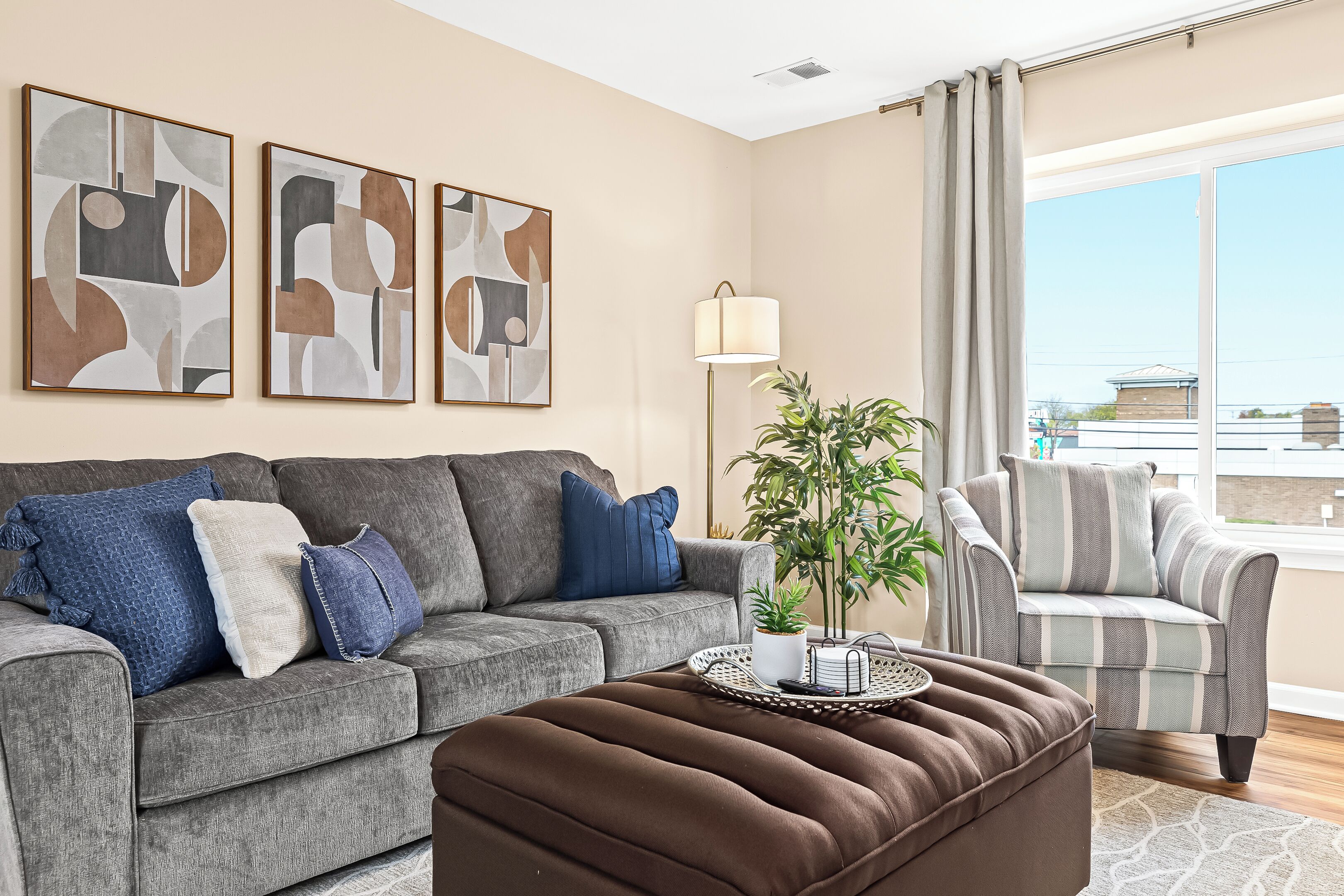 A living room with a grey sofa, a striped armchair, a brown ottoman, and abstract wall art.