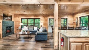 A spacious cabin interior with a living area featuring a sofa, coffee table, and fireplace. - NEW BUILD SEPT 2023 4 KINGS 1Q BUNK HOT TUB GAME ROOM THEATER  (Pigeon Forge)