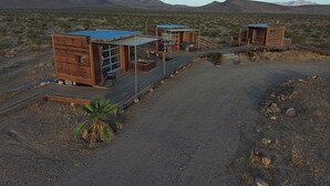 A desert landscape with three wooden cabins connected by a wooden deck.