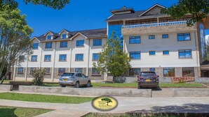 A multi-story hotel with a modern architectural design, featuring a mix of balconies and large windows. - Juniper Green Gardens Resort (Mweiga)