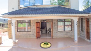 A hotel entrance with a covered patio, stone walls, and large windows. - Juniper Green Gardens Resort (Mweiga)