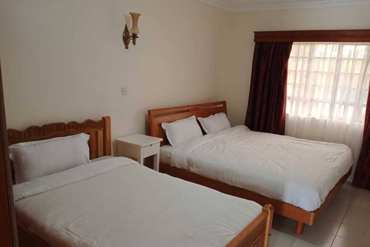 A hotel room with two single beds, a nightstand, a lamp, and a window with curtains.