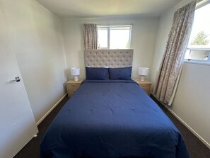 Une chambre à coucher avec un grand lit, une tête de lit, deux tables de chevet et une fenêtre avec des rideaux.