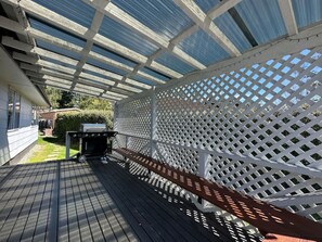 Una terraza cubierta al aire libre con una parrilla, una cerca de celosía blanca y un piso de madera.
