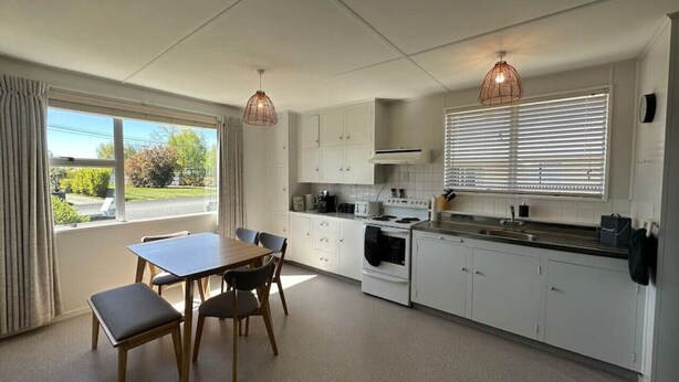 Une cuisine moderne avec des meubles blancs, une table à manger avec des chaises et des luminaires suspendus.