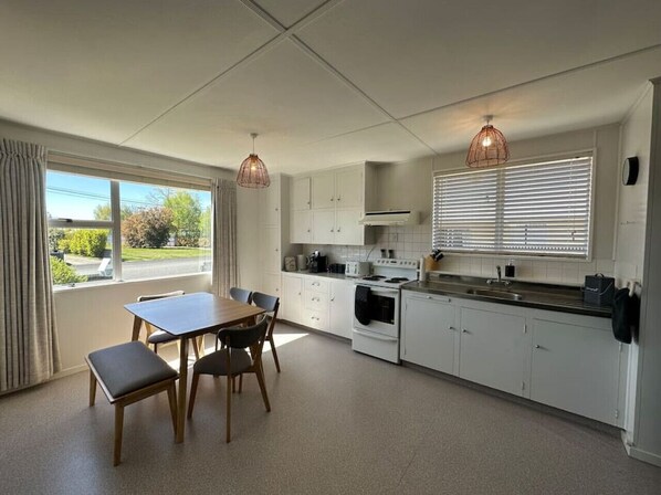 Une cuisine moderne avec des meubles blancs, une table à manger avec des chaises et des luminaires suspendus.