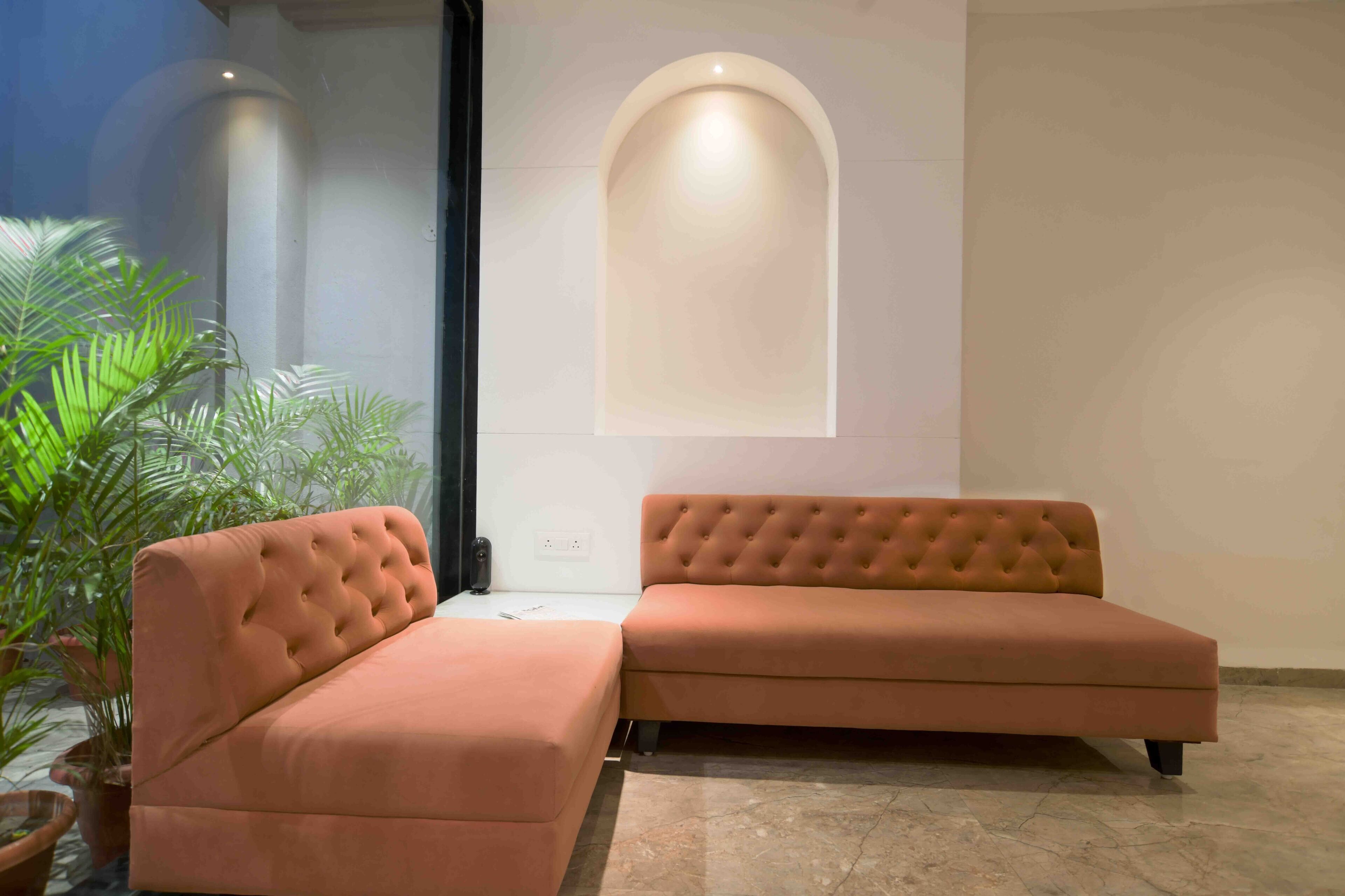 A modern living room with a sectional sofa and a built-in bench, a large arched window, and potted plants.