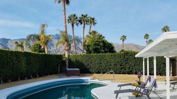 Une piscine à bord incurvé, entourée de palmiers et avec une chaîne de montagnes en arrière-plan.