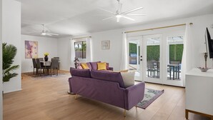 Un vaste espace de vie agrémenté d’un canapé violet, de parquet, de ventilateurs de plafond et d’un coin repas avec une table et des chaises.