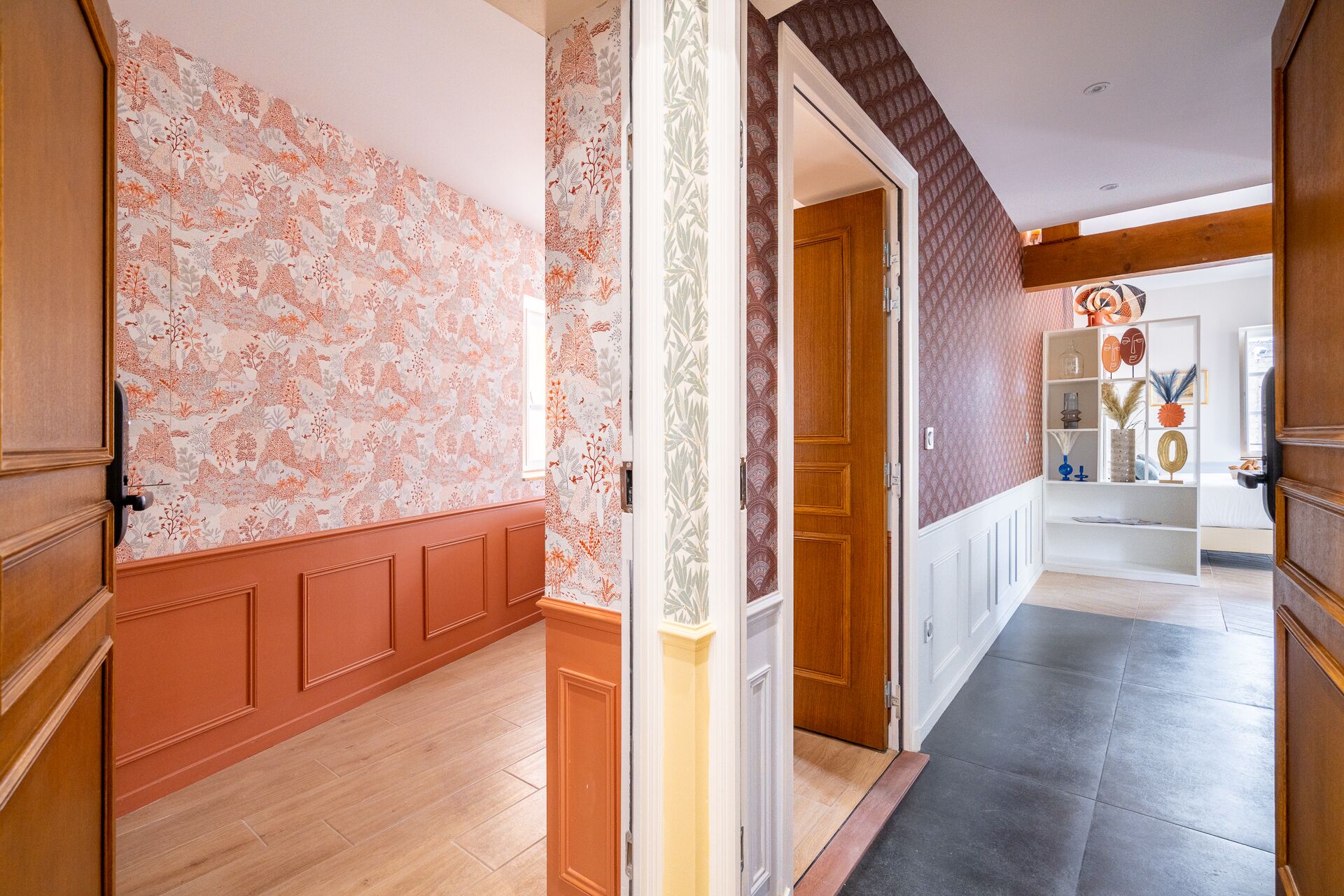 A hallway with patterned wallpaper, wooden doors, and a tiled floor.