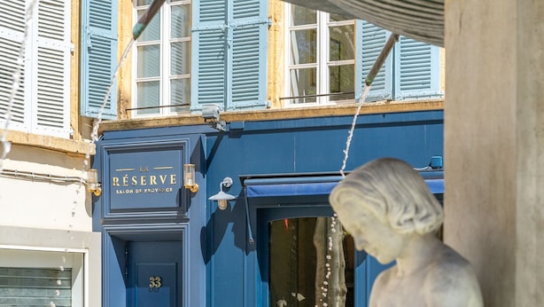 Una estatua de una figura sentada junto a un edificio con una puerta azul que dice "LA RESERVE".