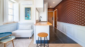 Una cocina moderna con encimera blanca, un taburete de madera y un cuadro en la pared.