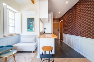 Une cuisine moderne avec un plan de travail blanc, un tabouret en bois et un tableau accroché au mur.