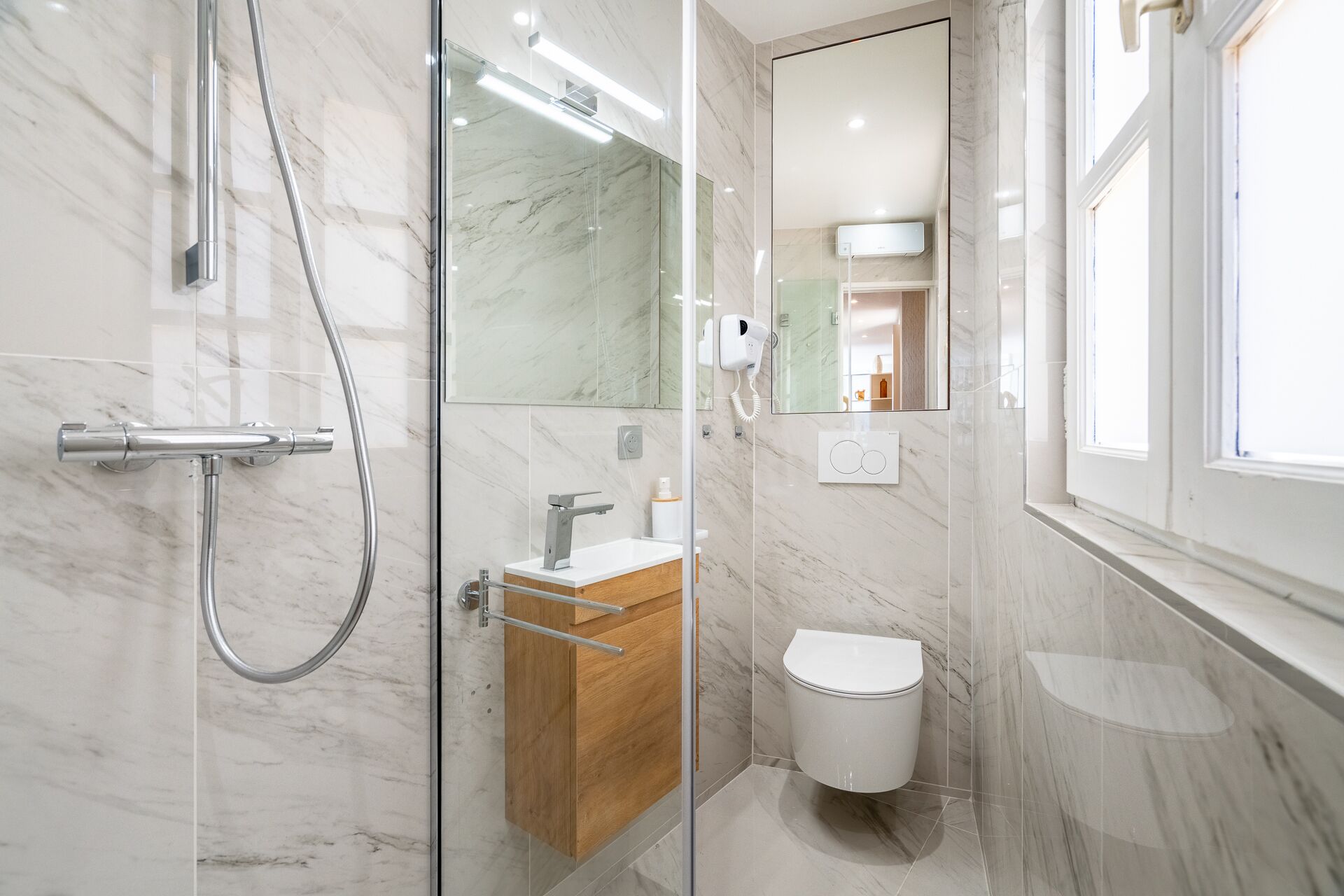 Une salle de bain moderne avec une douche à parois de verre, un meuble-lavabo en bois, des toilettes et un grand miroir.
