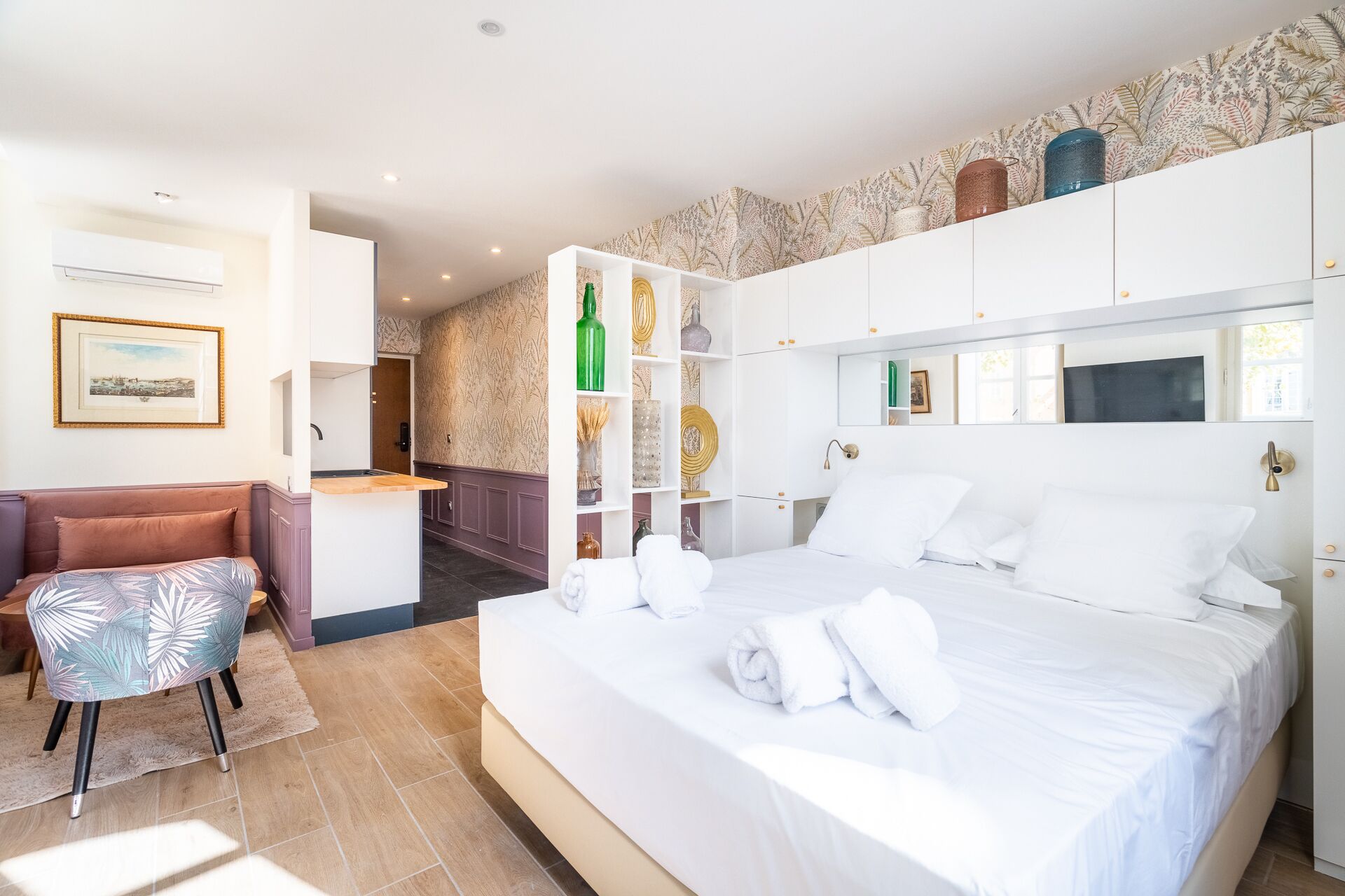 A modern hotel room with a large bed, a small seating area, and a kitchenette.