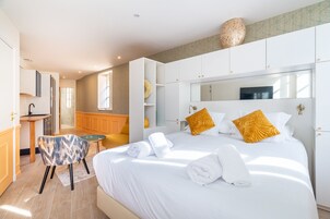 Une chambre d’hôtel moderne dotée d’un grand lit, d’un petit coin salon, d’une kitchenette et d’une salle de bain.